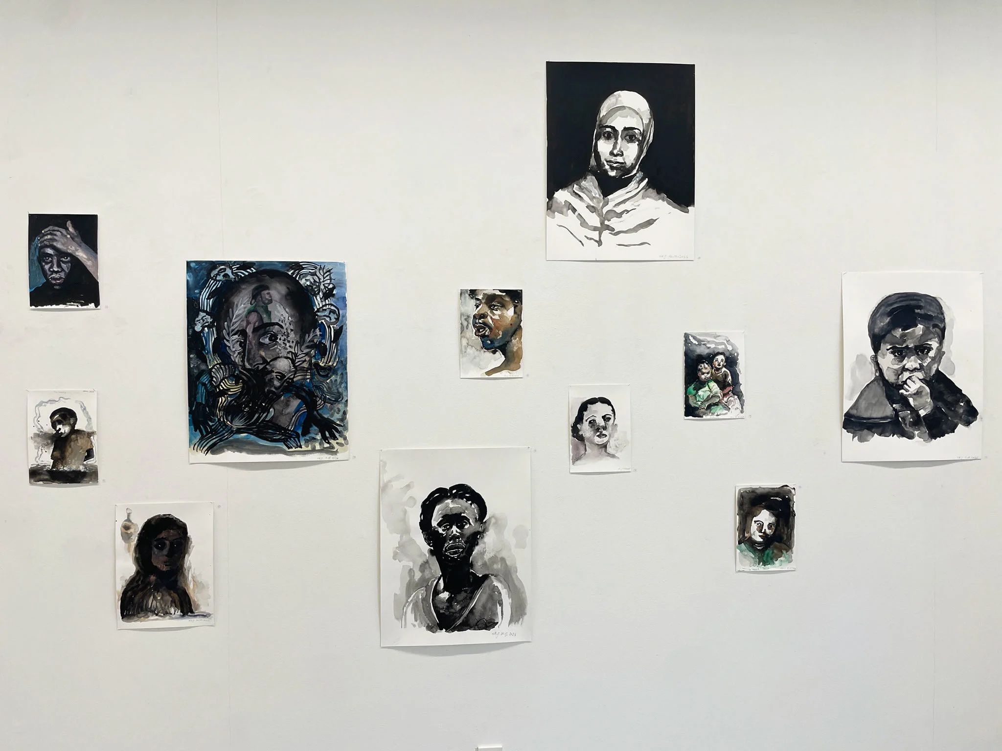 A gallery wall hung with a loose grid of watercolour portraits of different sizes