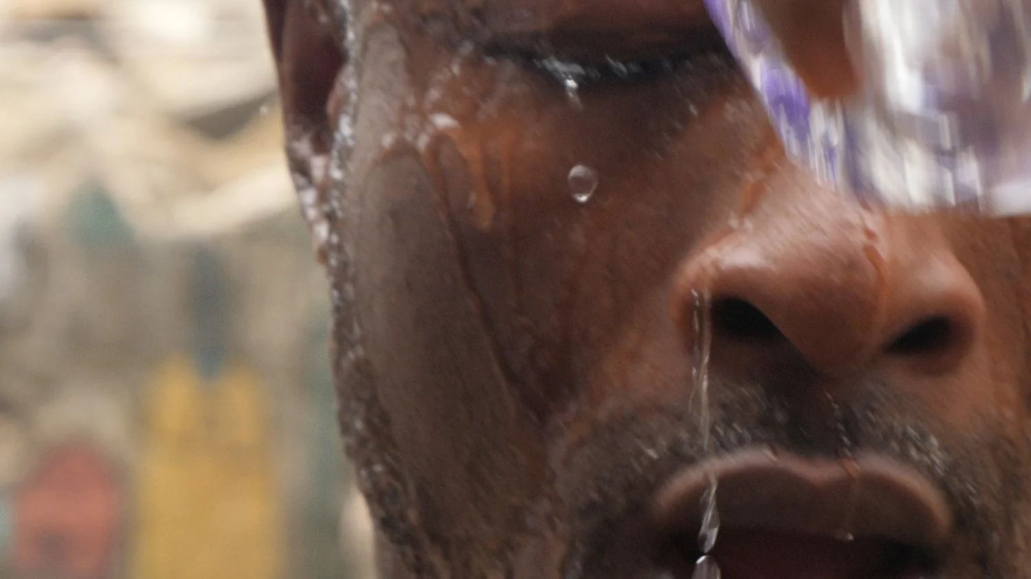 Close-up of a man’s face with water running down it, in a still from MUSCLE
